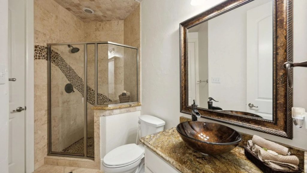 Warm-toned guest bathroom with stone shower and glass vessel sink.