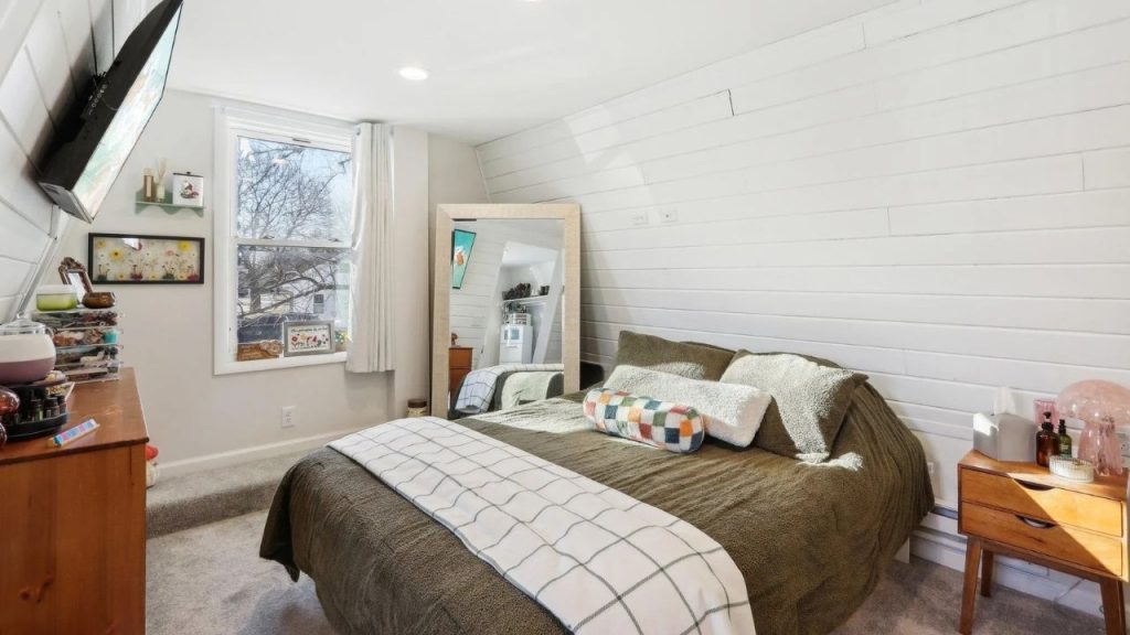 Charming bedroom with sloped ceiling, cozy bedding, and a large mirror.