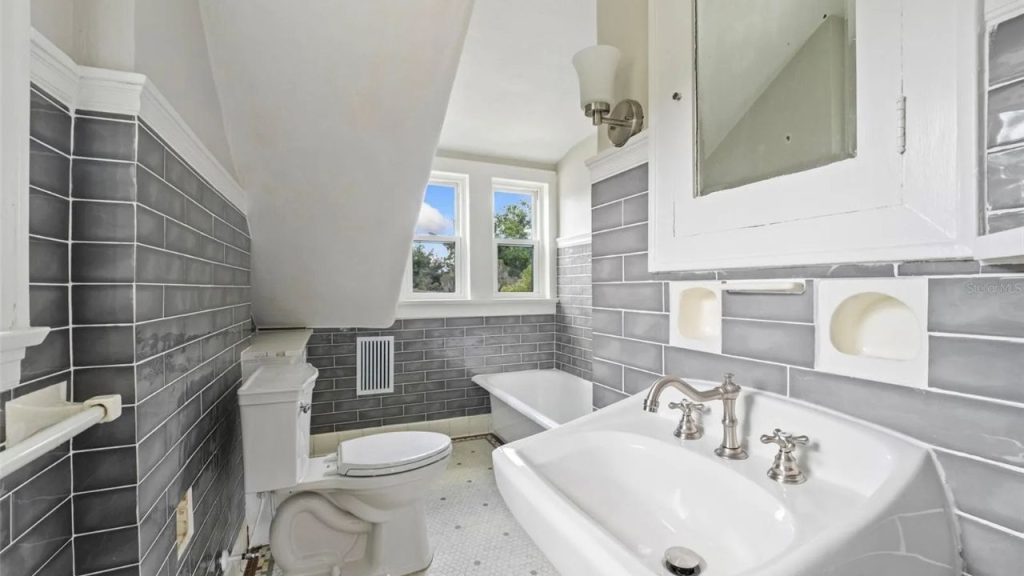 Small bathroom with gray tile, sloped ceiling, and clawfoot tub.