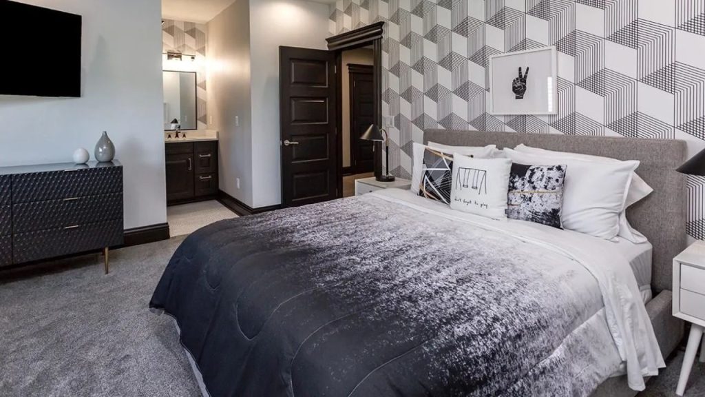 A modern bedroom with geometric wallpaper, a plush bed, mounted TV, and large windows, offering a stylish and cozy retreat.