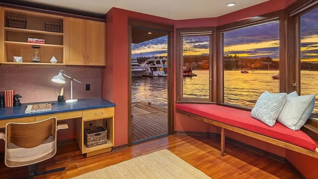 Home office with desk and window seat overlooking a marina at sunset.