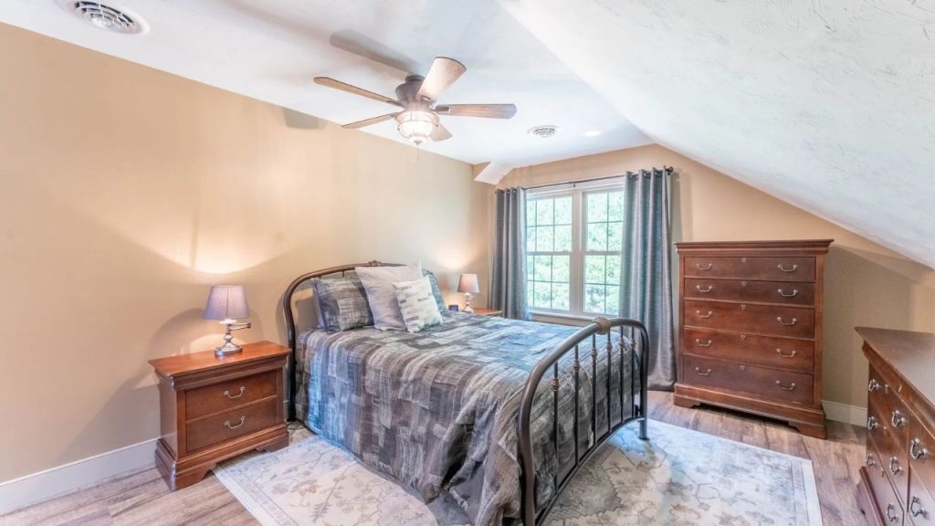 Cozy bedroom with sloped ceiling, metal bed frame, and wooden furniture.