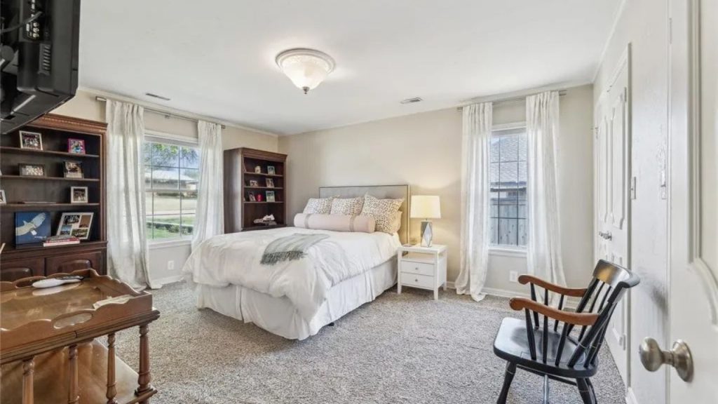 Bright and cozy bedroom with neutral decor, tall windows, and classic furniture.