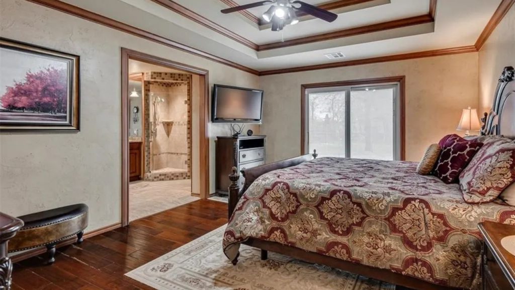 Cozy master bedroom with a plush bed, ceiling fan, TV, and view of an en-suite bathroom, featuring hardwood floors.