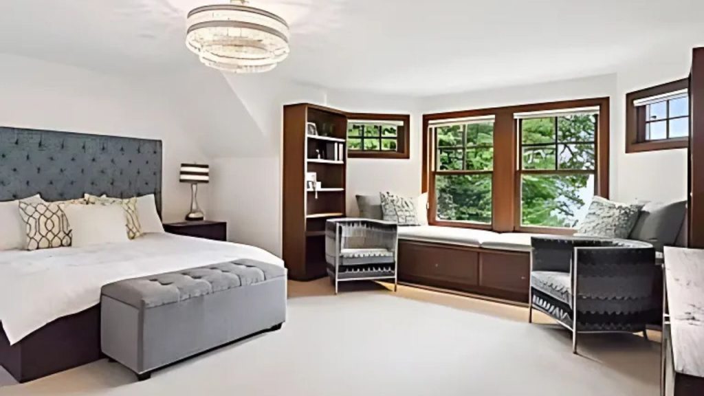 A chic bedroom with a window seat, chandelier, and tufted bed.