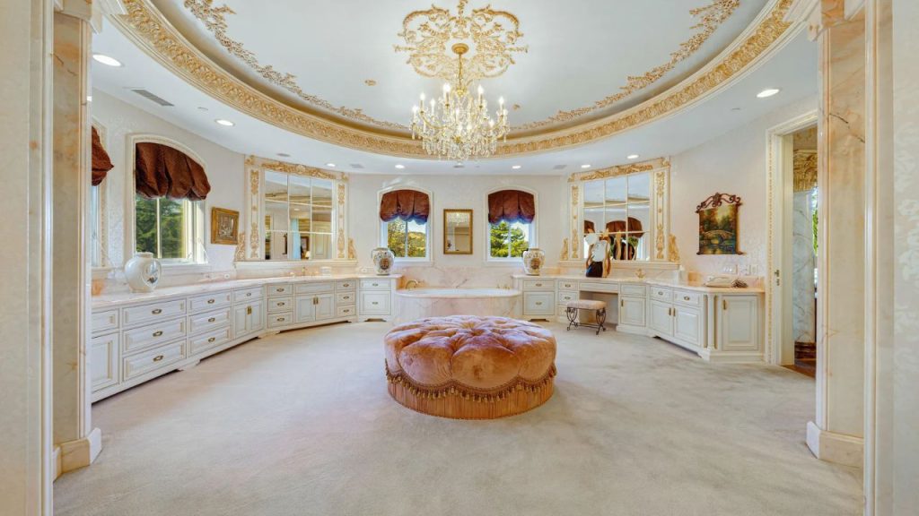 A spacious master suite with a chandelier, ottoman, and ornate cabinetry.
