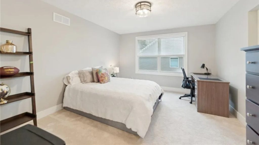 A cozy bedroom with a bed, desk, and shelves near large windows.