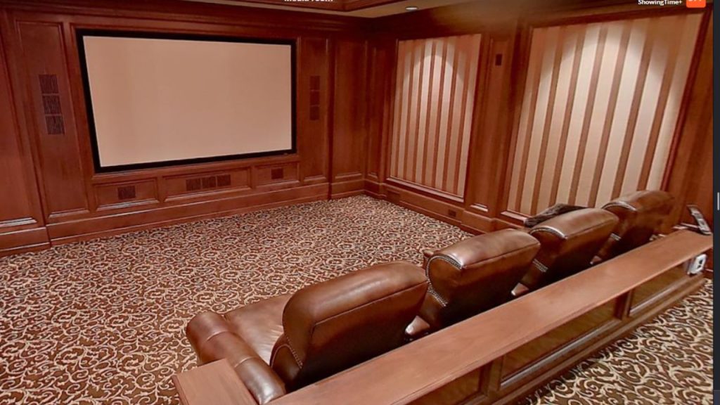 A cozy media room with leather recliners, a large screen, wooden paneling, and a patterned carpet.