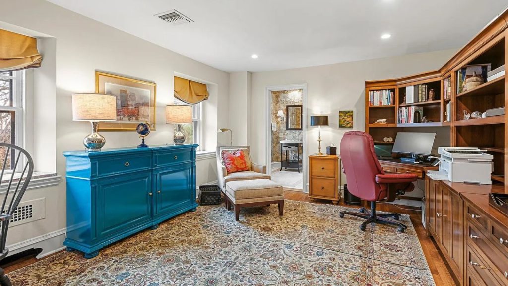 A cozy home office with a blue cabinet, red chair, and large windows.