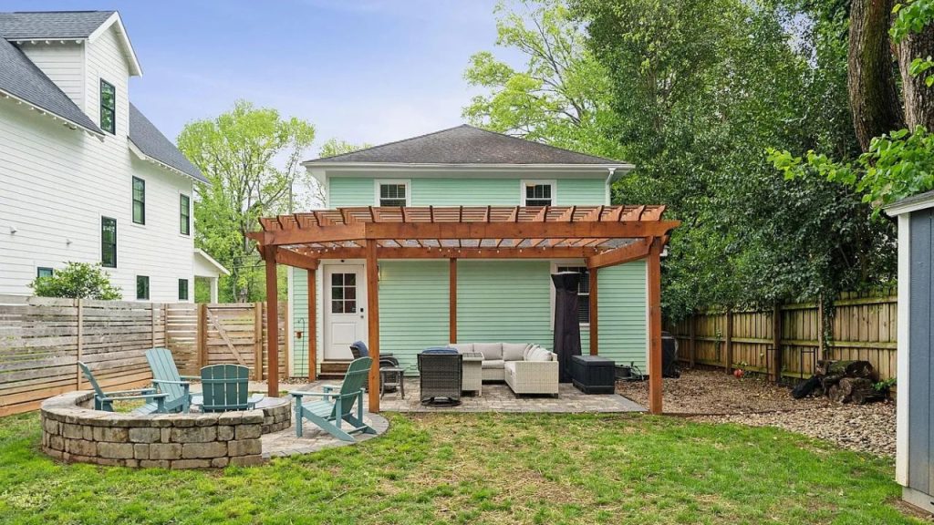 A backyard with a pergola, wicker furniture, and a stone fire pit.