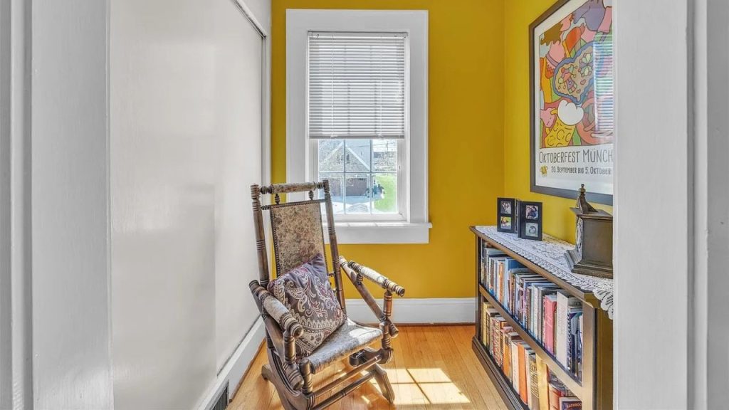 A cozy reading nook with a yellow room, rocking chair, bookshelf, and sunny window.