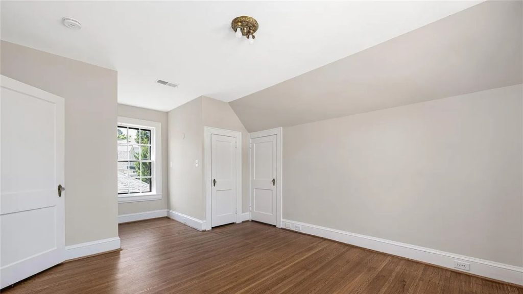 A bright bedroom with a slanted ceiling, large window, and hardwood floors.
