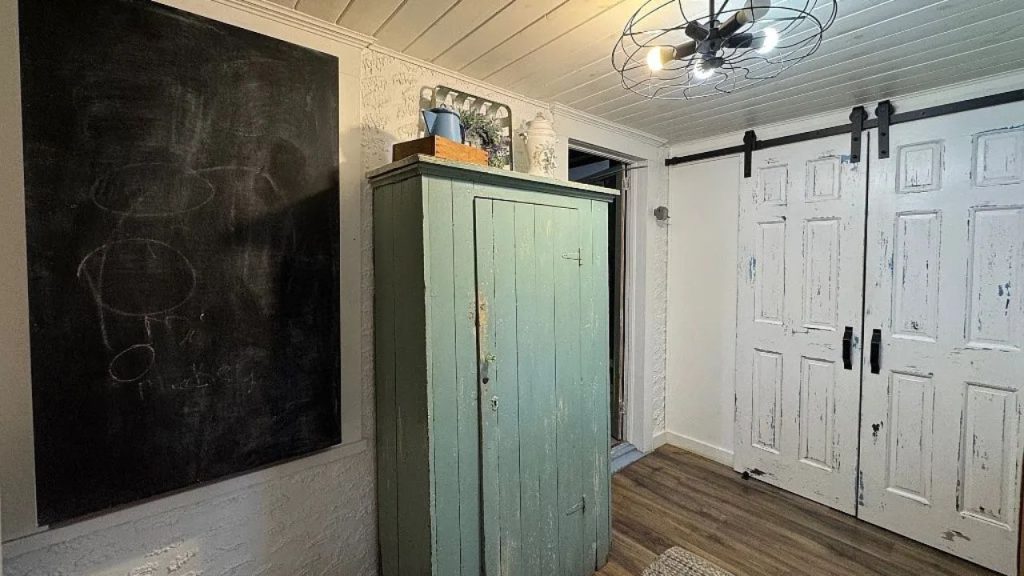 A rustic storage nook with a teal cabinet, sliding barn doors, and a chalkboard on a brick wall.