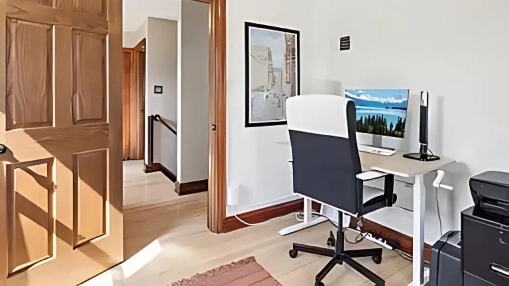 A quiet home office with a white desk, black chair, and scenic monitor view.