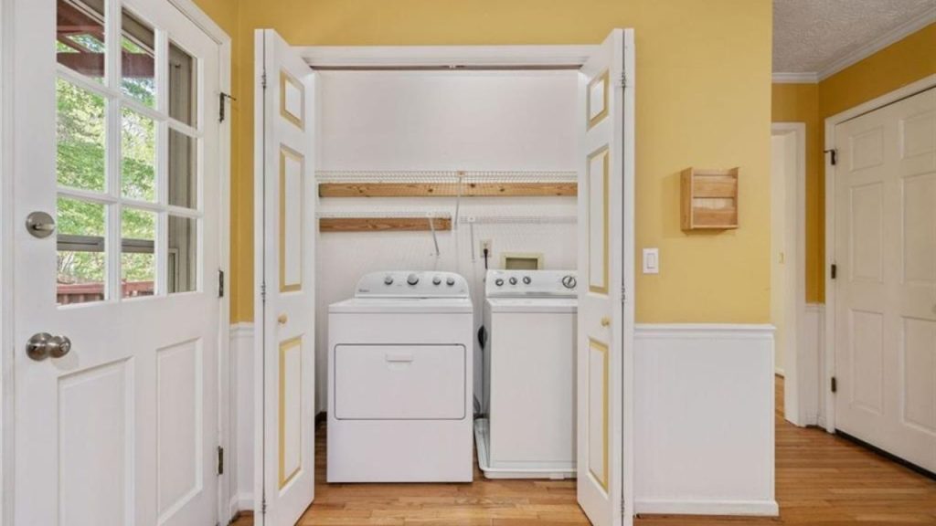 A cozy laundry room with yellow walls, white washer and dryer, wooden shelf, and a windowed door.