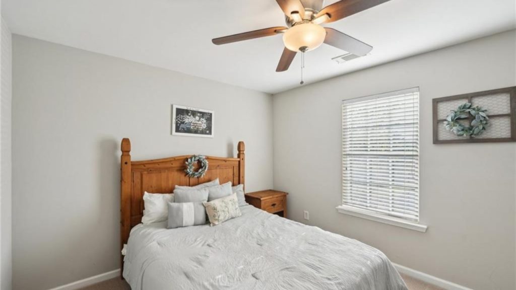 A calm bedroom with a wooden bed, gray bedding, ceiling fan, and large windows.