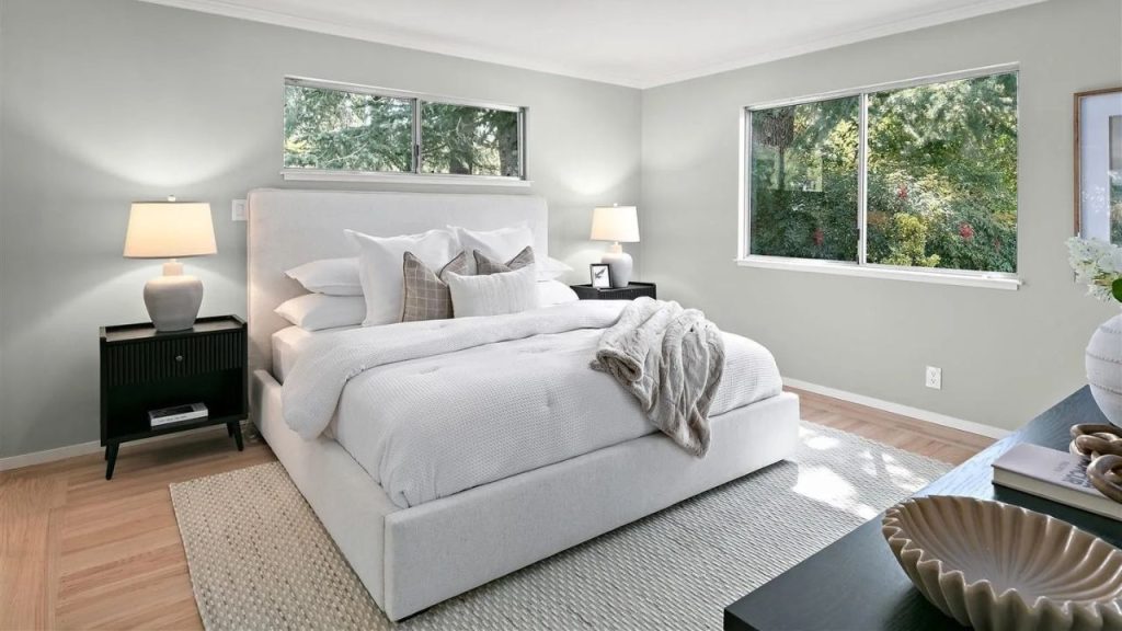 A calm master bedroom with a white bed, green views, and warm lighting from stylish lamps.