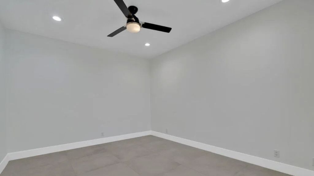 A minimalist bedroom with gray walls, a ceiling fan, and large tile flooring.