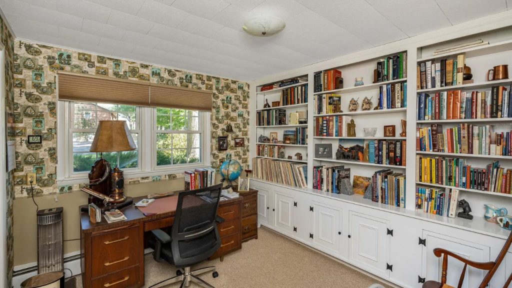 Cozy home office with built-in bookshelves, large windows, and vintage wallpaper.