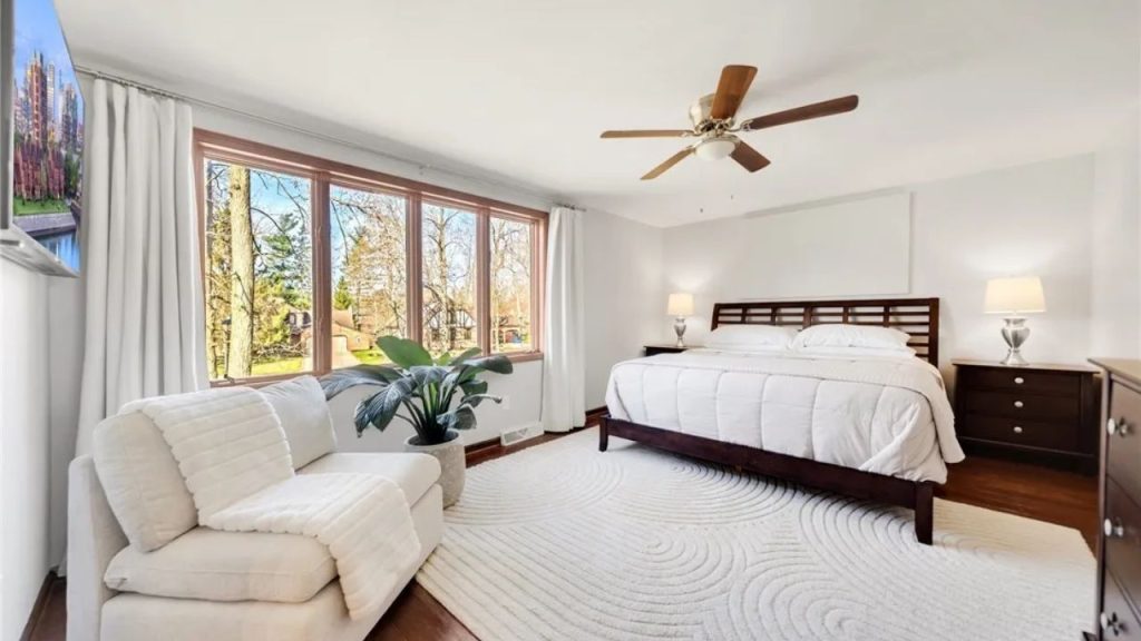 Spacious bedroom with large window, white rug, and dark wood bed.