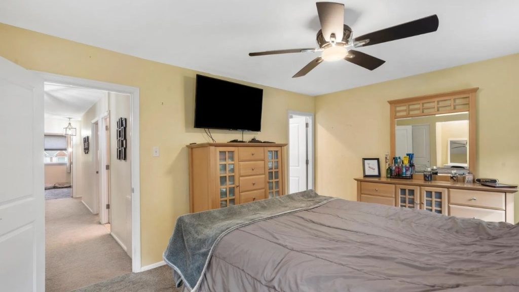 Bedroom with light wood furniture, wall-mounted TV, and hallway view.