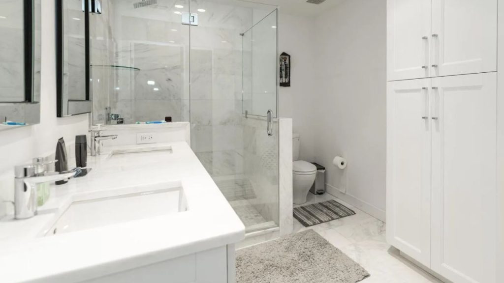 Marble bathroom with double sinks, glass shower, and tall storage cabinet.