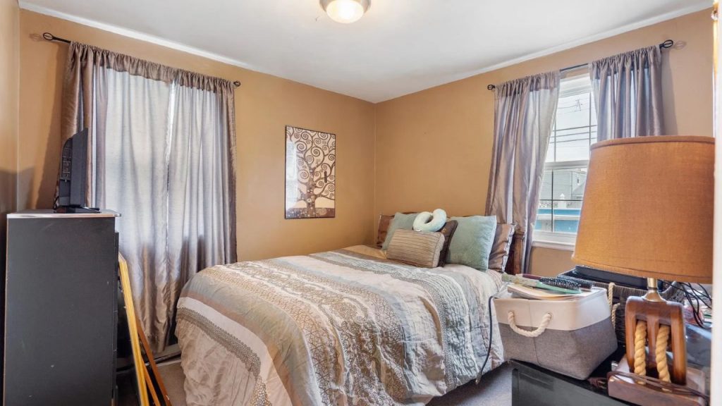 Small bedroom with tan walls, soft lighting, and a neatly made bed.