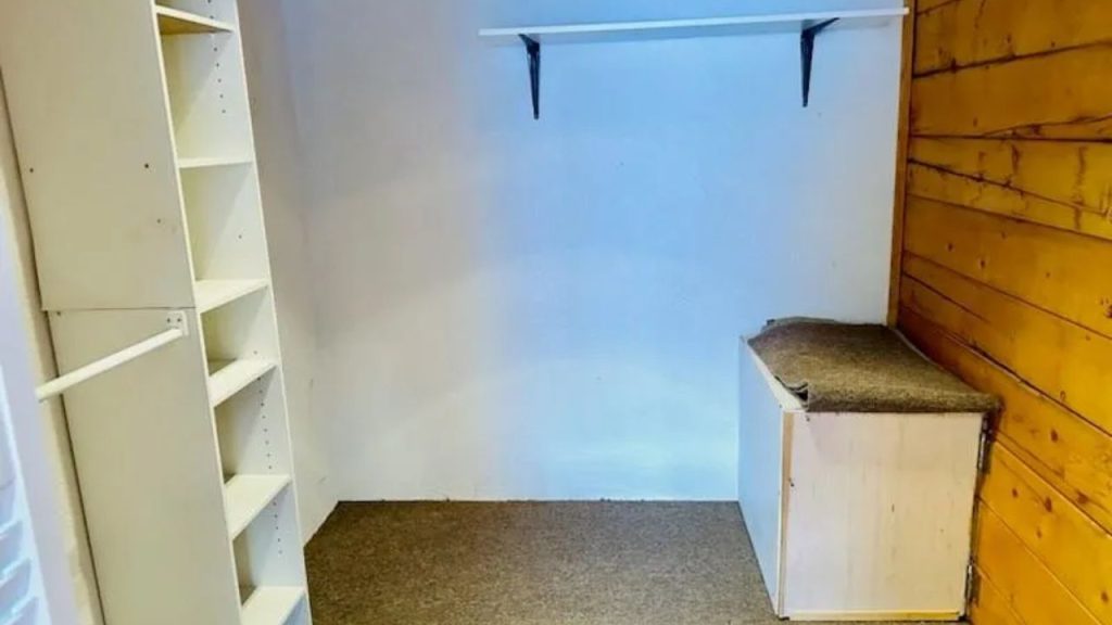 Walk-in closet with open shelves, bench, and wood accent wall.