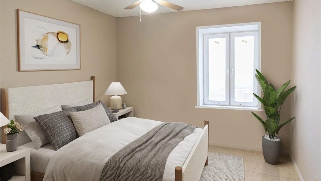 A calm bedroom with beige walls, gray bed, potted plant, white lamp, and abstract artwork.