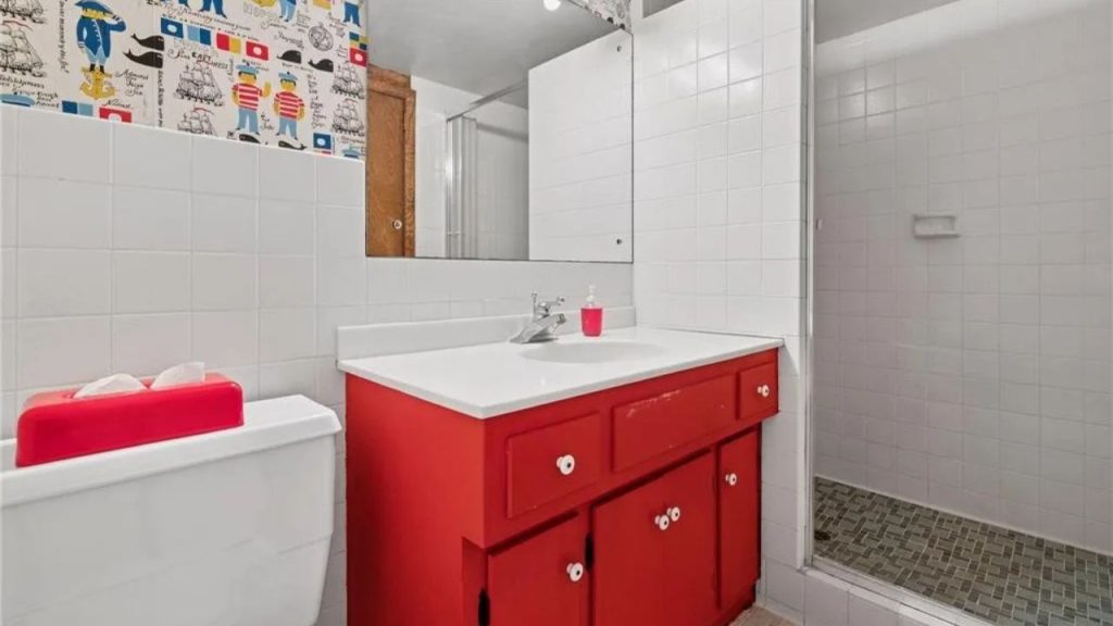 Lively bathroom with red vanity and nautical wallpaper.