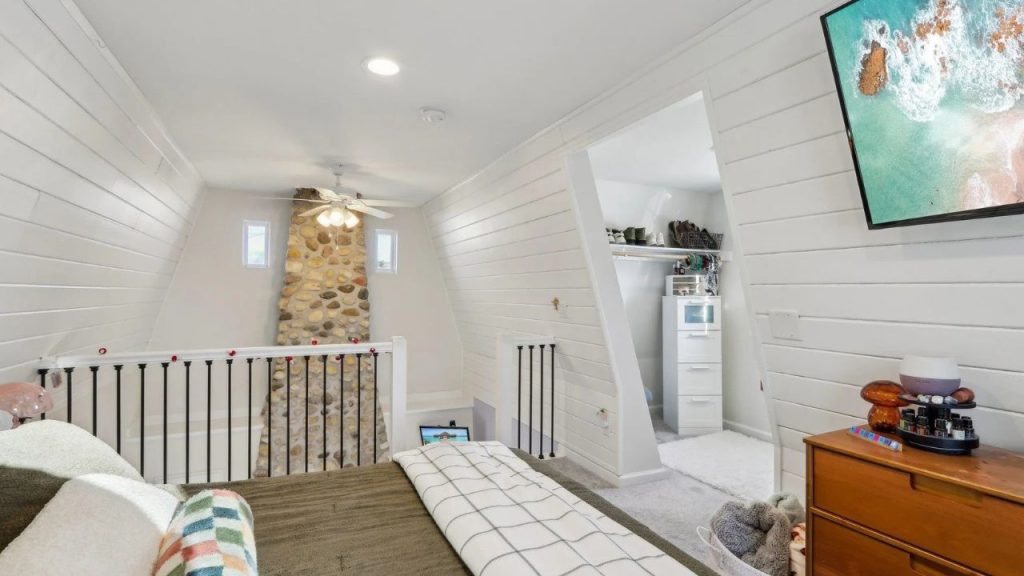 Loft bedroom with white shiplap walls, stone chimney, and hidden walk-in closet.
