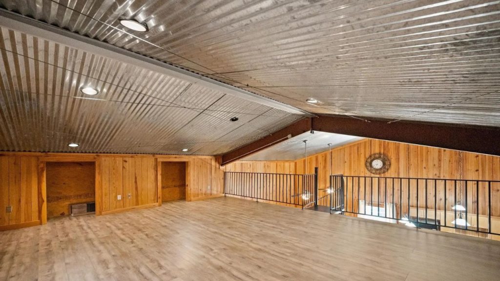 Open loft with wood walls and metal ceiling overlooking living room.
