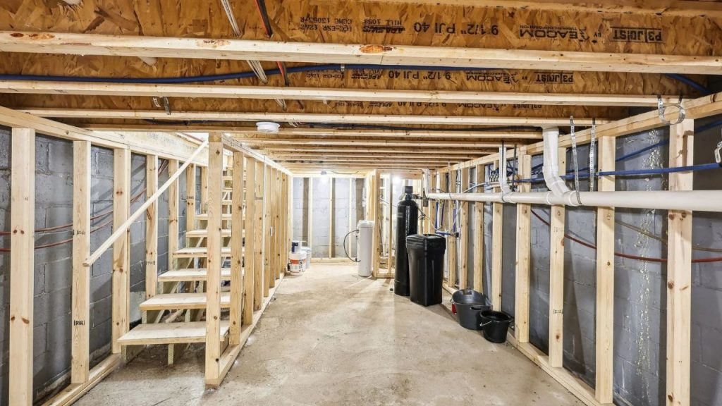Unfinished basement with exposed framing, utilities, and wood stairs.