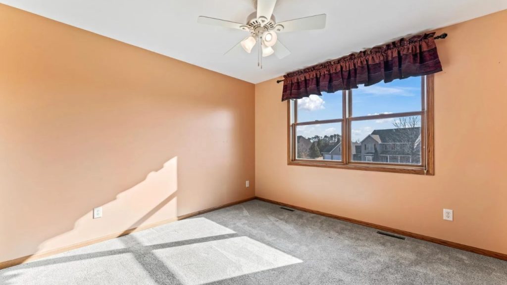 Sunny upstairs room with window, fan, and peach walls.