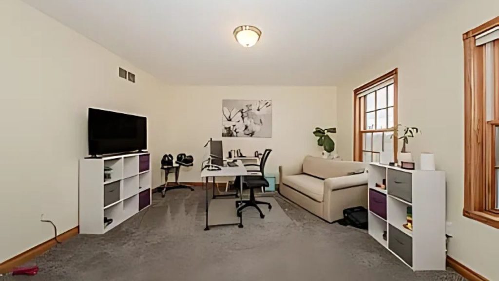 Bright home office with two desks, a beige couch, and wall-mounted TV.