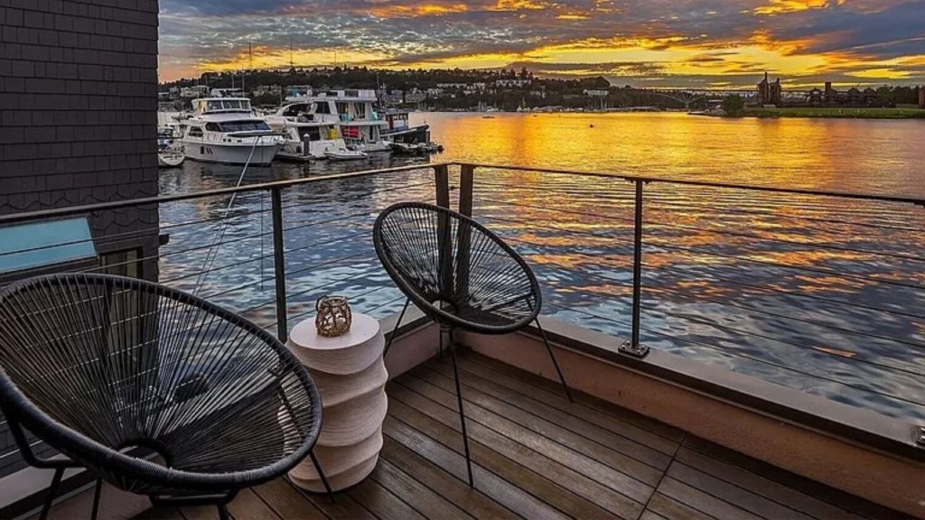 Balcony with modern chairs overlooking a lake at sunset.