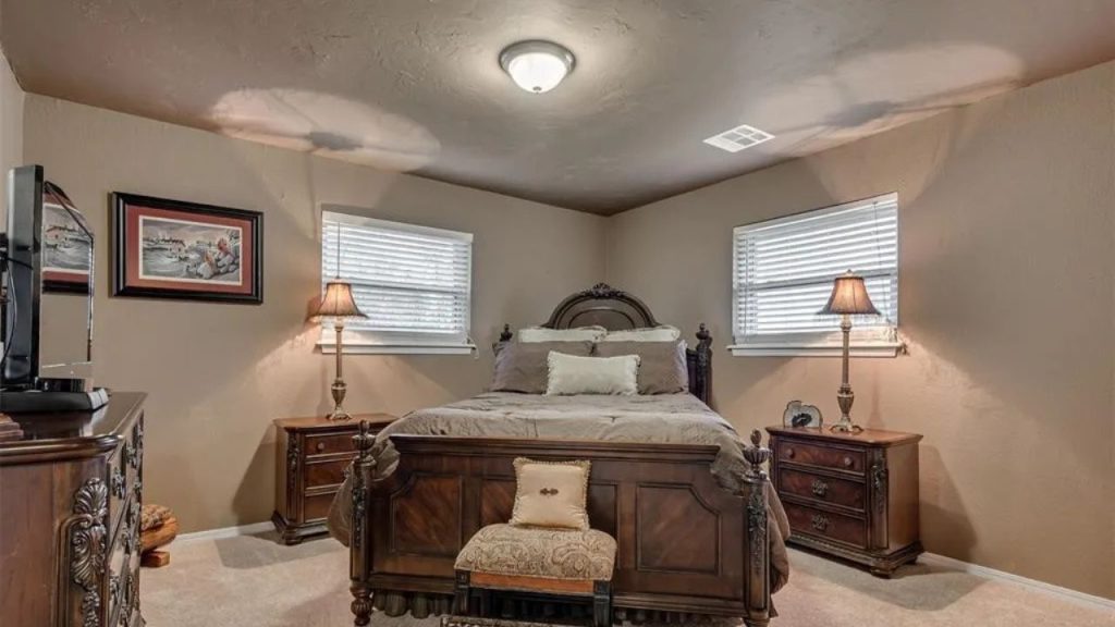 Cozy guest bedroom with a wooden bed, bedside lamps, and windows, featuring soft carpet and a TV dresser.