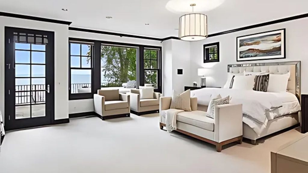 A bright bedroom with lake views, a tufted bed, and beige armchairs.