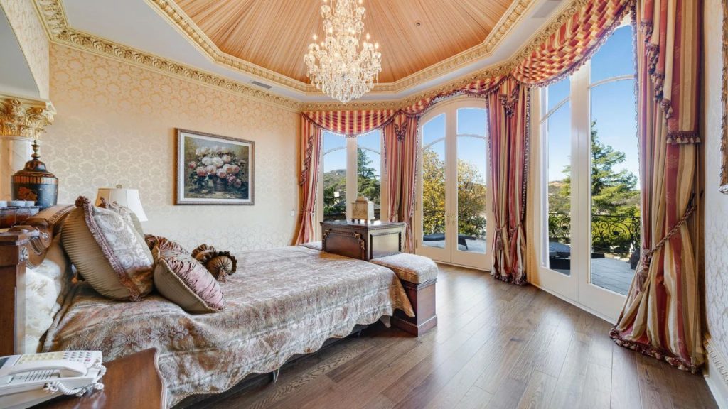 A serene bedroom with a chandelier, ornate bed, and large windows.