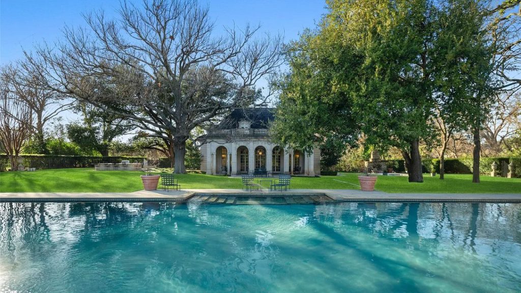 A poolside pavilion with arched windows and a serene pool surrounded by trees.