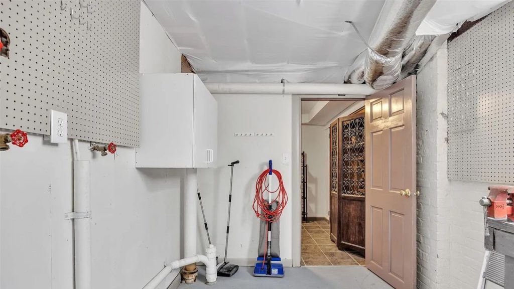 A functional utility room with pegboards, a vacuum, brooms, and a view of a wine cellar in a basement setting.