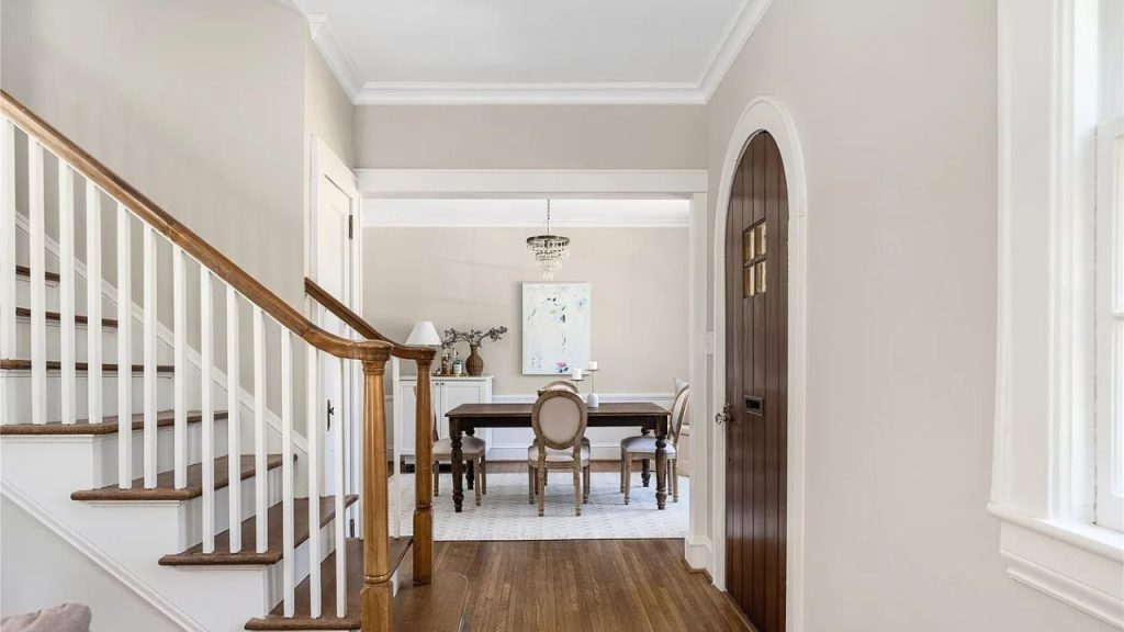 A bright foyer with a wooden staircase and view into a dining area.