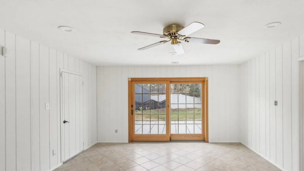 A spacious family room with wooden sliding doors, tiled floor, and a ceiling fan, featuring white paneling.