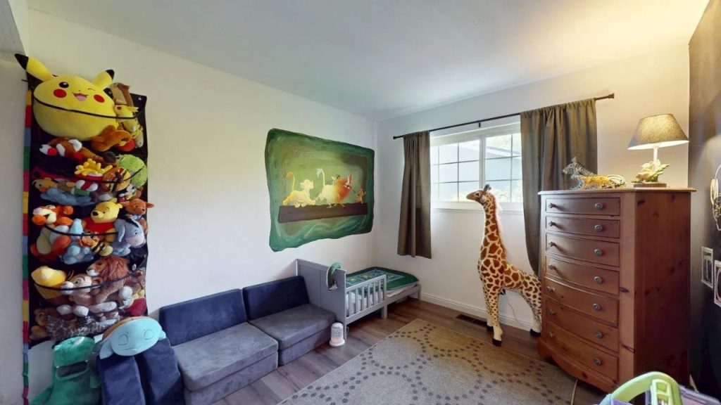 A lively kid’s room with a Lion King mural, giraffe statue, gray couch, stuffed toys, and wooden dresser.