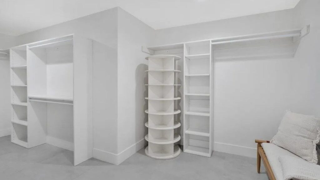 A spacious walk-in closet with white shelving, a rotating shoe rack, and a cozy bench.