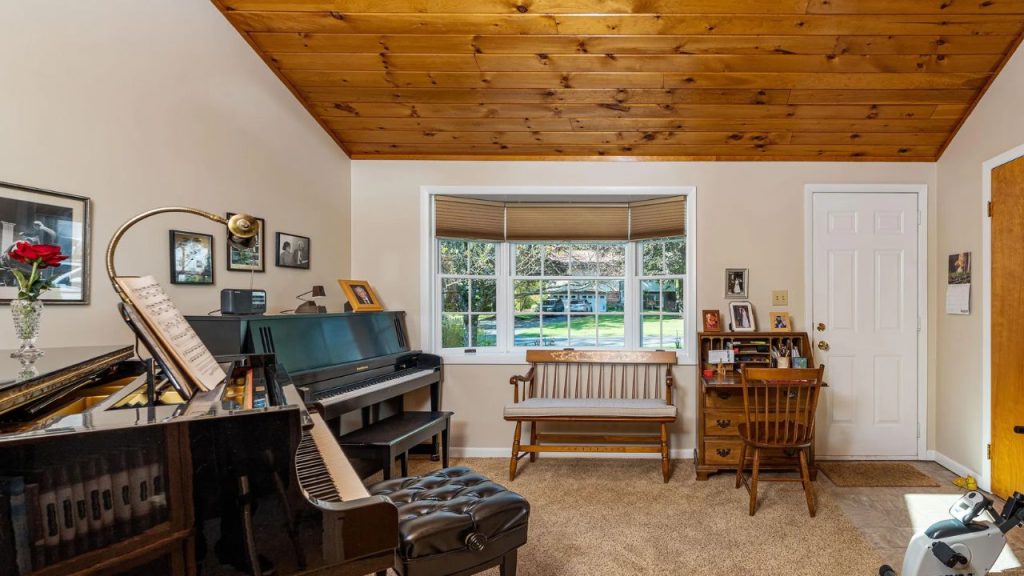 Cozy music room with pianos, wood ceiling, and bay window.
