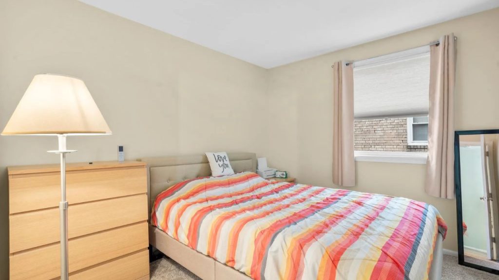 Small bedroom with colorful bedspread, light wood furniture, and a window.