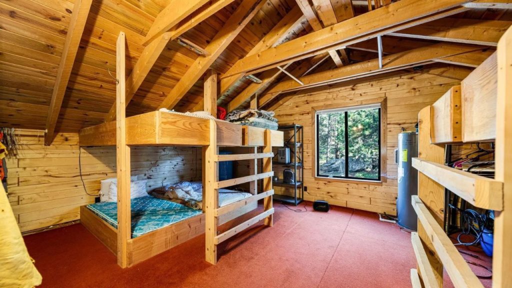 Loft with wood walls, bunk beds, and forest views through large window.