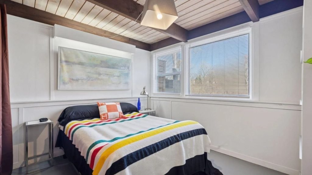 Guest bedroom with striped blanket and wood ceiling.