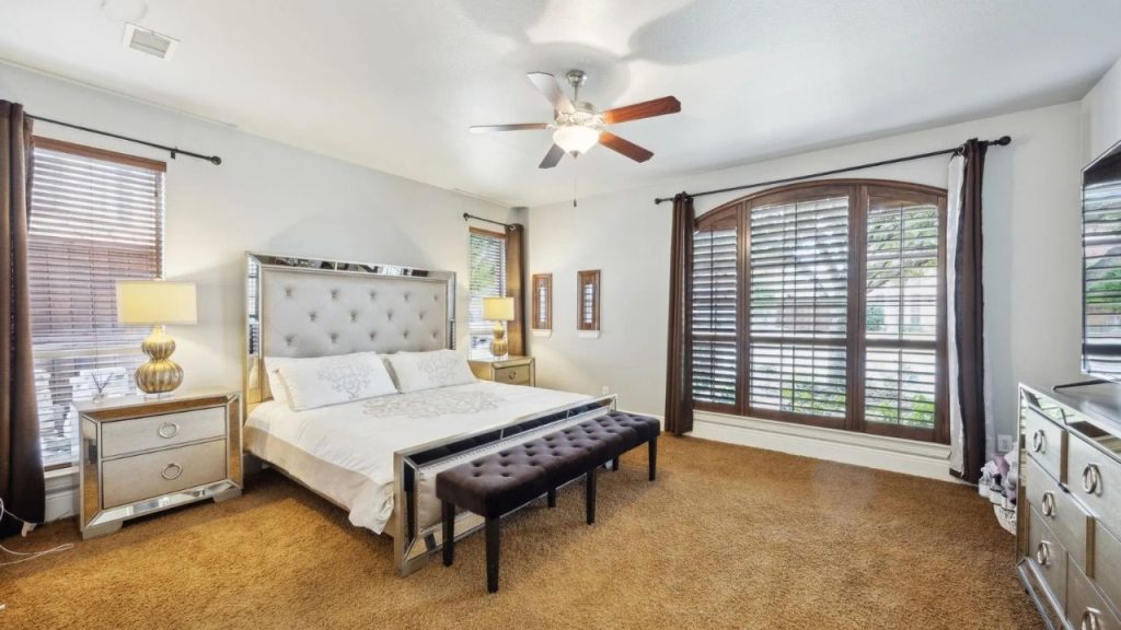 Cozy bedroom with tufted bed, mirrored furniture, and large wooden shutters.
